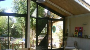 A room with a wooden table and chairs, a sofa, and a view of an outdoor area with a wooden deck and greenery. - Mansion - Ploemeur (Ploemeur)