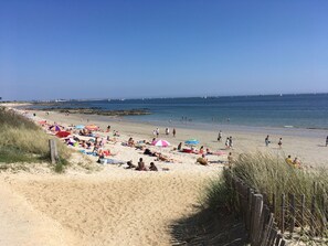 Ein Strand mit badenden Personen, einer Holzlattenveranda und blauem Himmel.