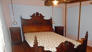 Un lit traditionnel en bois, à colonnes, surmonté d’une couvre-lit à motifs floraux, flanqué de deux tables de chevet avec des lampes, dans une pièce au plancher en bois et aux murs d’une couleur claire et unie.