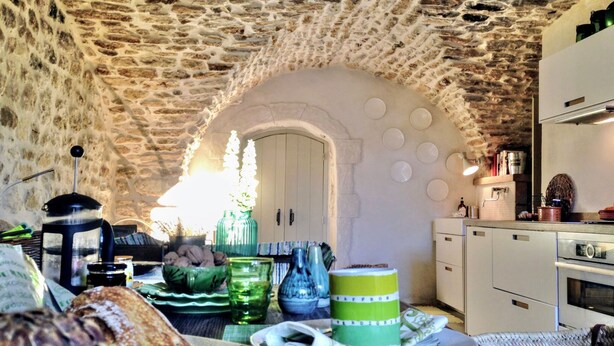 A rustic kitchen with stone walls, a wooden table with breakfast items, and a white refrigerator.