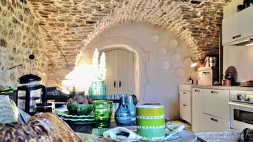 A rustic kitchen with stone walls, a wooden table with breakfast items, and a white refrigerator.