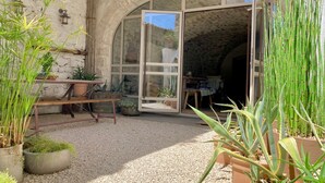 A rustic stone building with a large arched doorway leading to a room. There are potted plants and a wooden bench outside.