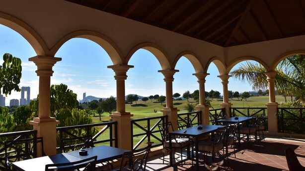 An outdoor patio with tables and chairs, a view of a golf course, and a city skyline in the distance. - Spacious modern villa - fabulous sea views, free WIFI, beach & golf (Golf Bahía)