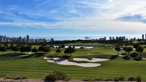 A golf course with sand bunkers, trees, and a city skyline in the background. - Spacious modern villa - fabulous sea views, free WIFI, beach & golf (Golf Bahía)
