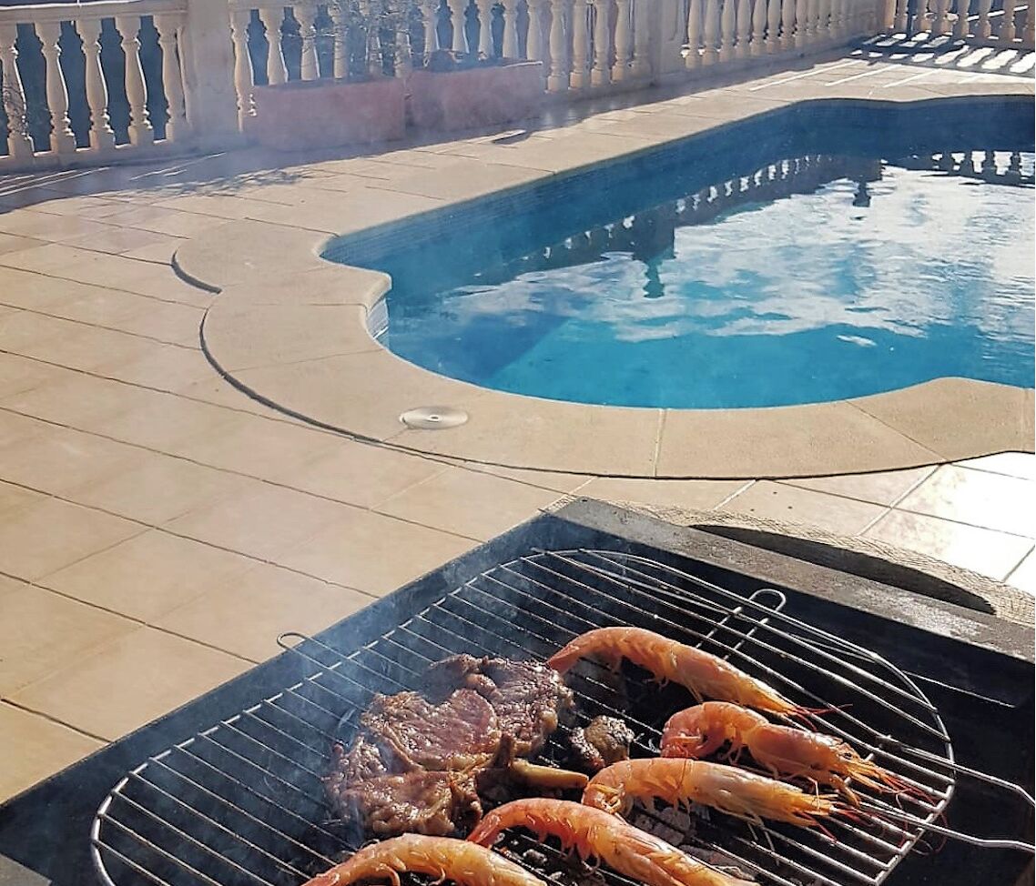 Zona junto a la piscina con una parrilla preparando camarones y filete.