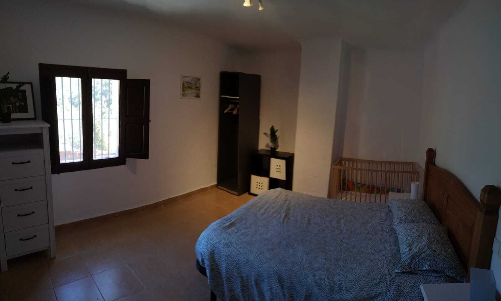 A bedroom with a bed, a dresser, a wardrobe, a window, and a crib.