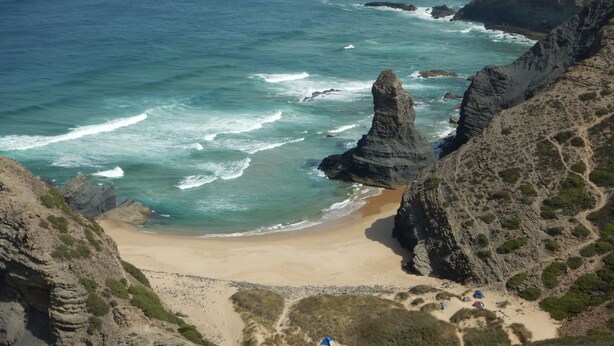 Un paysage côtier caractérisé par une formation rocheuse imposante, une plage de sable et quelques tentes.