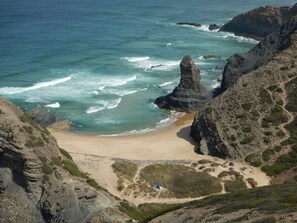 Un paisaje costero con una destacada formación rocosa, una playa arenosa y algunas tiendas de campaña.