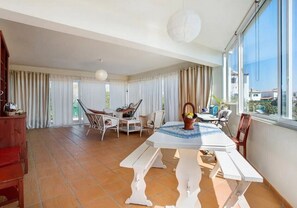 A spacious balcony with a white table and benches, surrounded by curtains and wicker chairs.