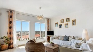 Un salon spacieux avec une grande fenêtre, un canapé, une table basse et un téléviseur.