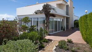Une maison moderne à deux étages, dotée de grandes fenêtres en verre, d’une allée pavée et d’un jardin bien entretenu.