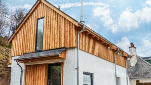 Een houten woonhuis met twee verdiepingen, een schuin dak, schoorsteen en een klein raam.