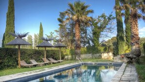 Une piscine entourée de chaises longues et de parasols, le tout bordé de grands arbres et de haies.