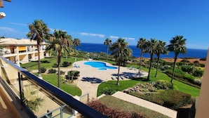 Zona de piscina con sillas de descanso, palmeras y vista al océano.