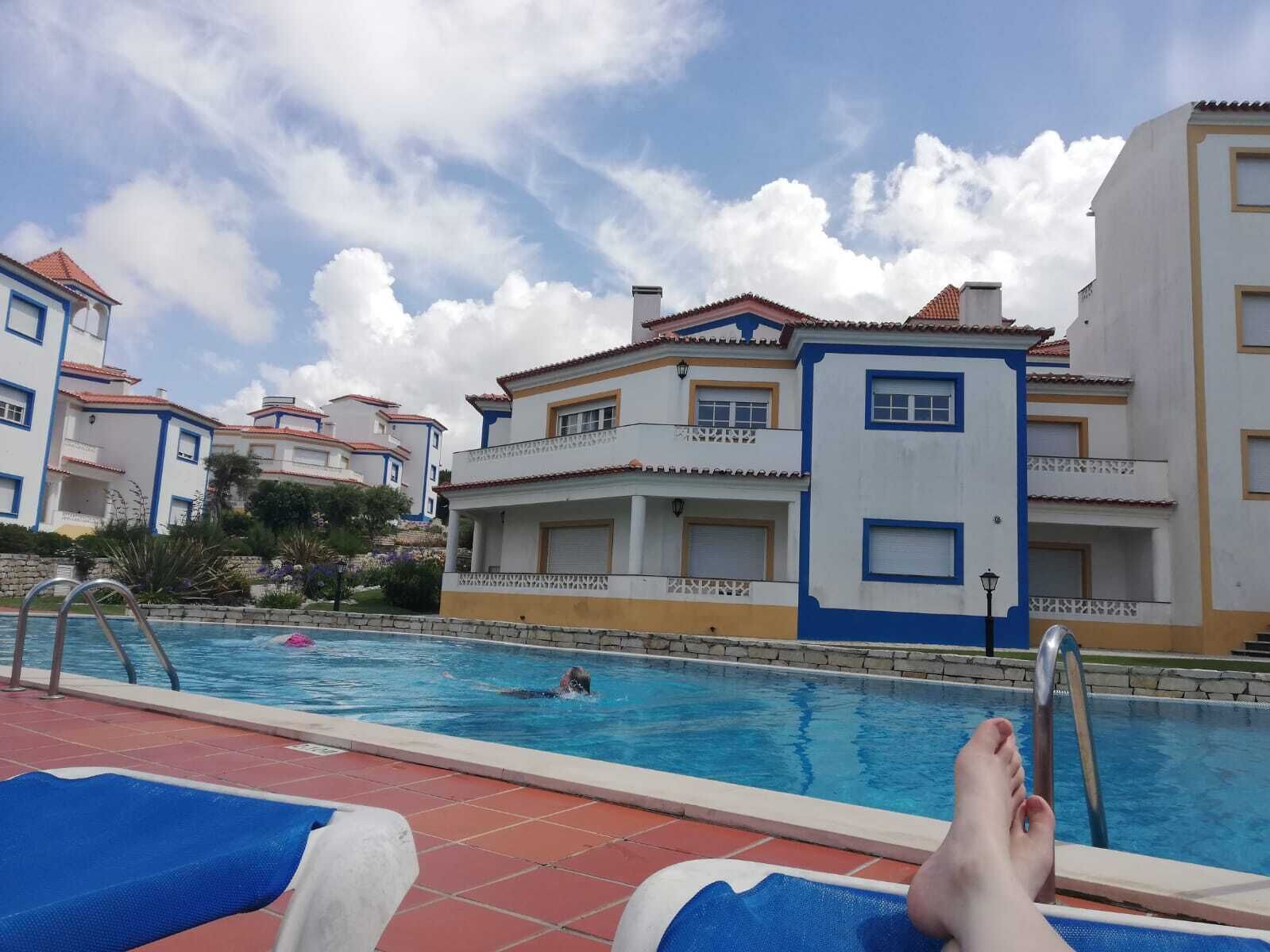 Une zone avec piscine, des chaises longues, une personne qui nage et, au fond, un bâtiment doté de balcons.