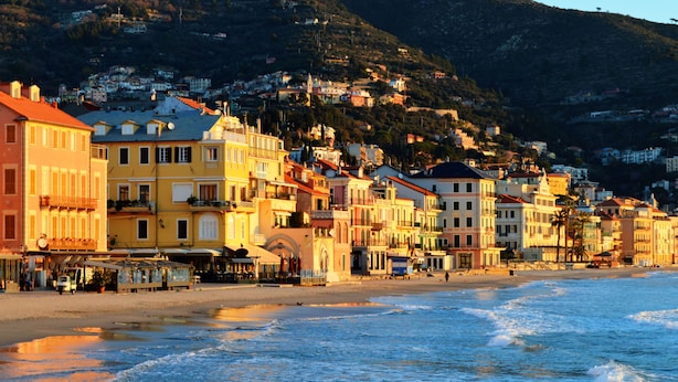 Une ville côtière aux bâtiments aux couleurs vives, bordée d’une plage, offrant une vue dégagée sur la mer et s’étendant au pied de montagnes.