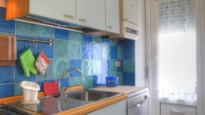 Une cuisine équipée d’un évier, d’une cuisinière et d’un lave-vaisselle. On y trouve des placards et une fenêtre avec un rideau.