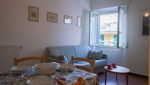 Un coin repas avec une table dressée pour quatre personnes, un canapé et une fenêtre donnant sur des immeubles.