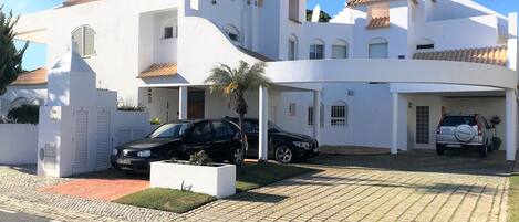 A modern white house with a curved driveway, a black car parked in the driveway, and a Honda SUV in the garage.
