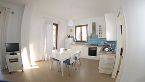 Een compacte keuken met witte kastjes, een zithoek met een tafel en stoelen, en een kleine tv op een standaard.