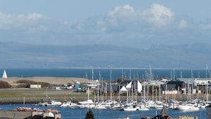 Ein Yachthafen mit zahlreichen Schiffen, ein Leuchtturm im Hintergrund und eine Küstenlandschaft.