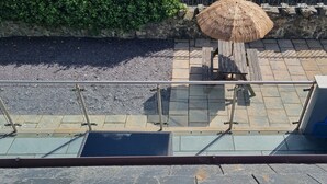 Ein Balkon mit Glasgeländer, einem Strohdachschirm und einer Steinmauer.