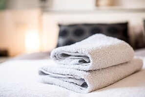 A neatly folded white towel stacked on a bed with a pillow in the background.