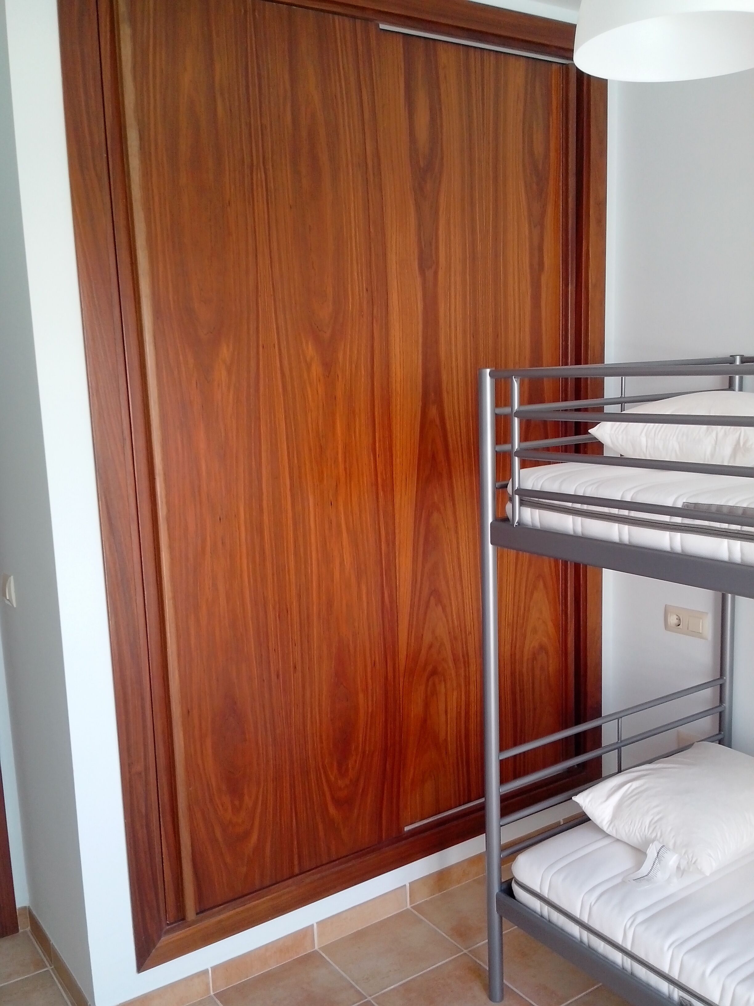 A bunk bed with white bedding in a room with wooden paneling and a white ceiling light.