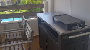 A balcony with a wooden bench, a small table, and a grill.