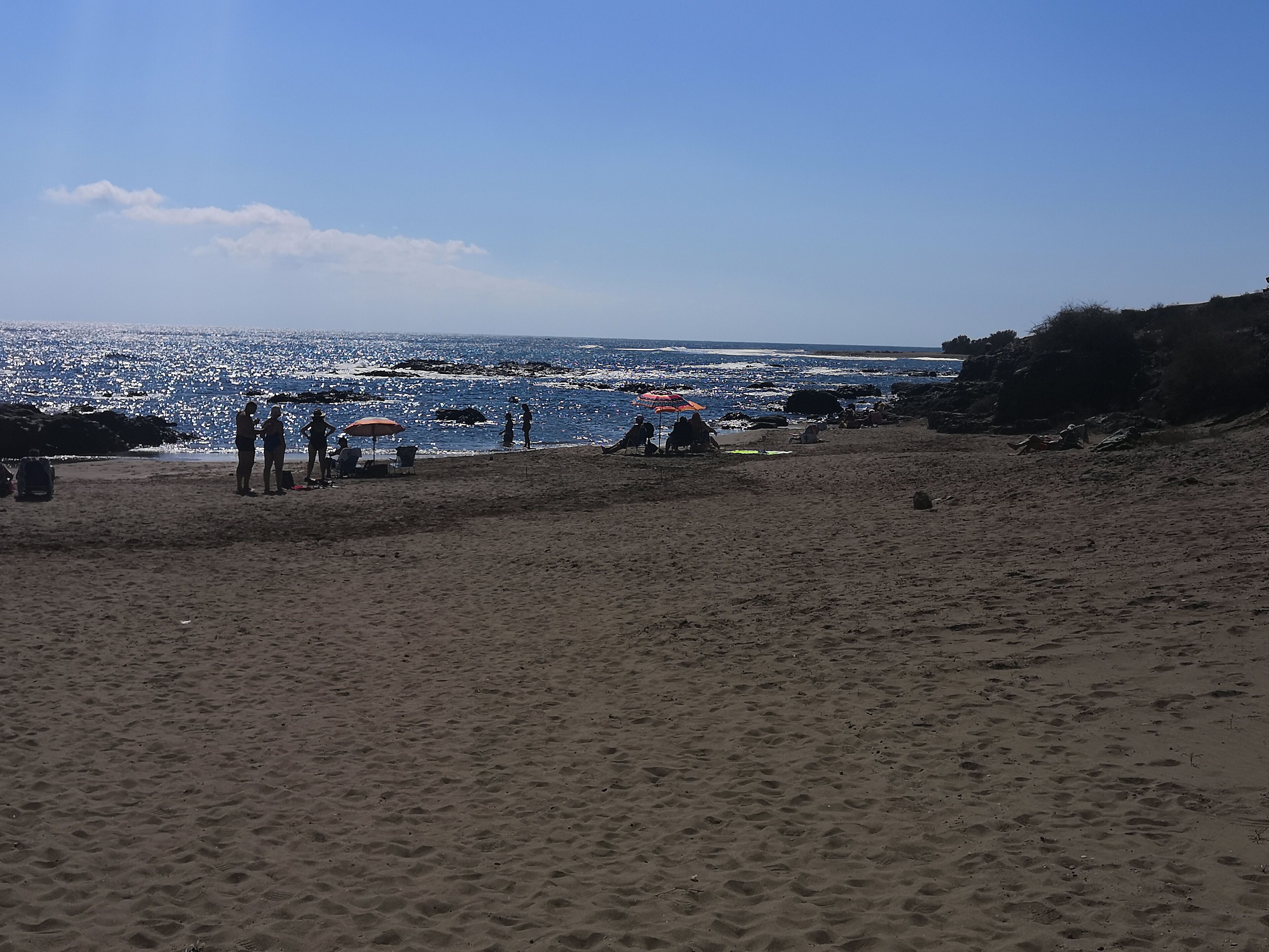 A beach with people, a chair, and an umbrella.