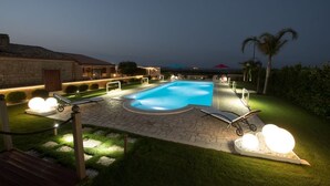 A well-lit swimming pool area with lounge chairs and a stone pathway. - Villa Fenicottero - A Charming Oasis in Nature (Ispica)