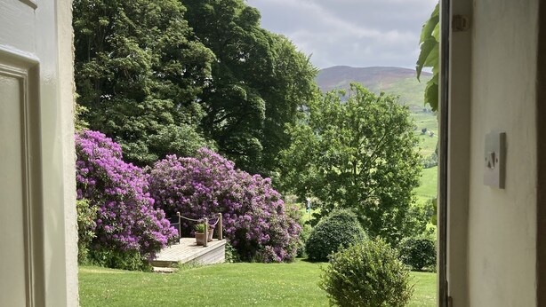A view through an open door into a garden with a lawn, a gravel path, and a potted plant. - Plas yn Yale, Llandegla with mountain views from all windows 4starVisitWales (Denbighshire)