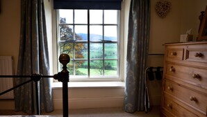 A bedroom with a large window, a wooden dresser, and a bed with floral bedding. - Plas yn Yale, Llandegla with mountain views from all windows 4starVisitWales (Denbighshire)