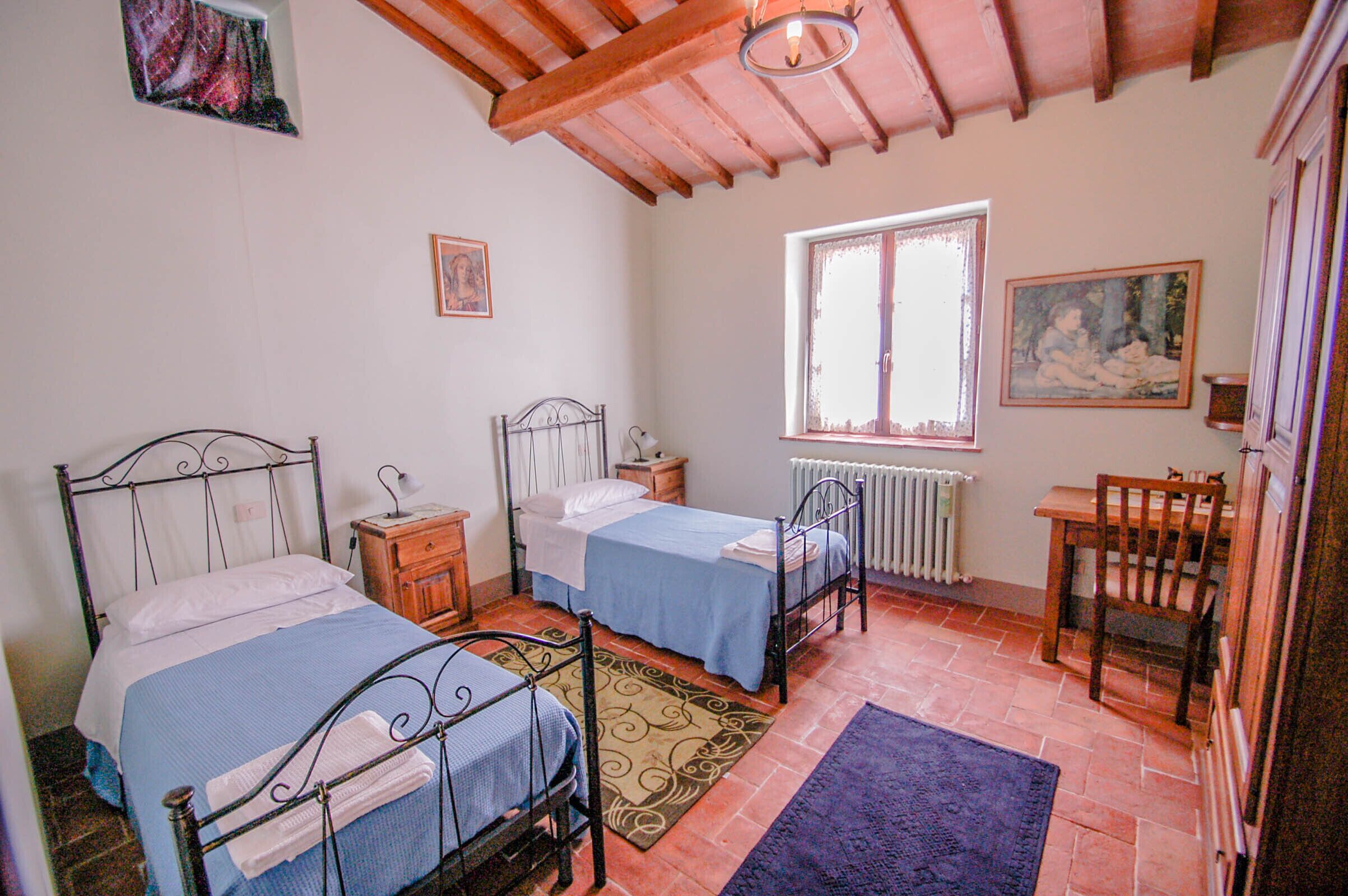 A bedroom with two single beds, a wooden table, a chair, a window, and a radiator.