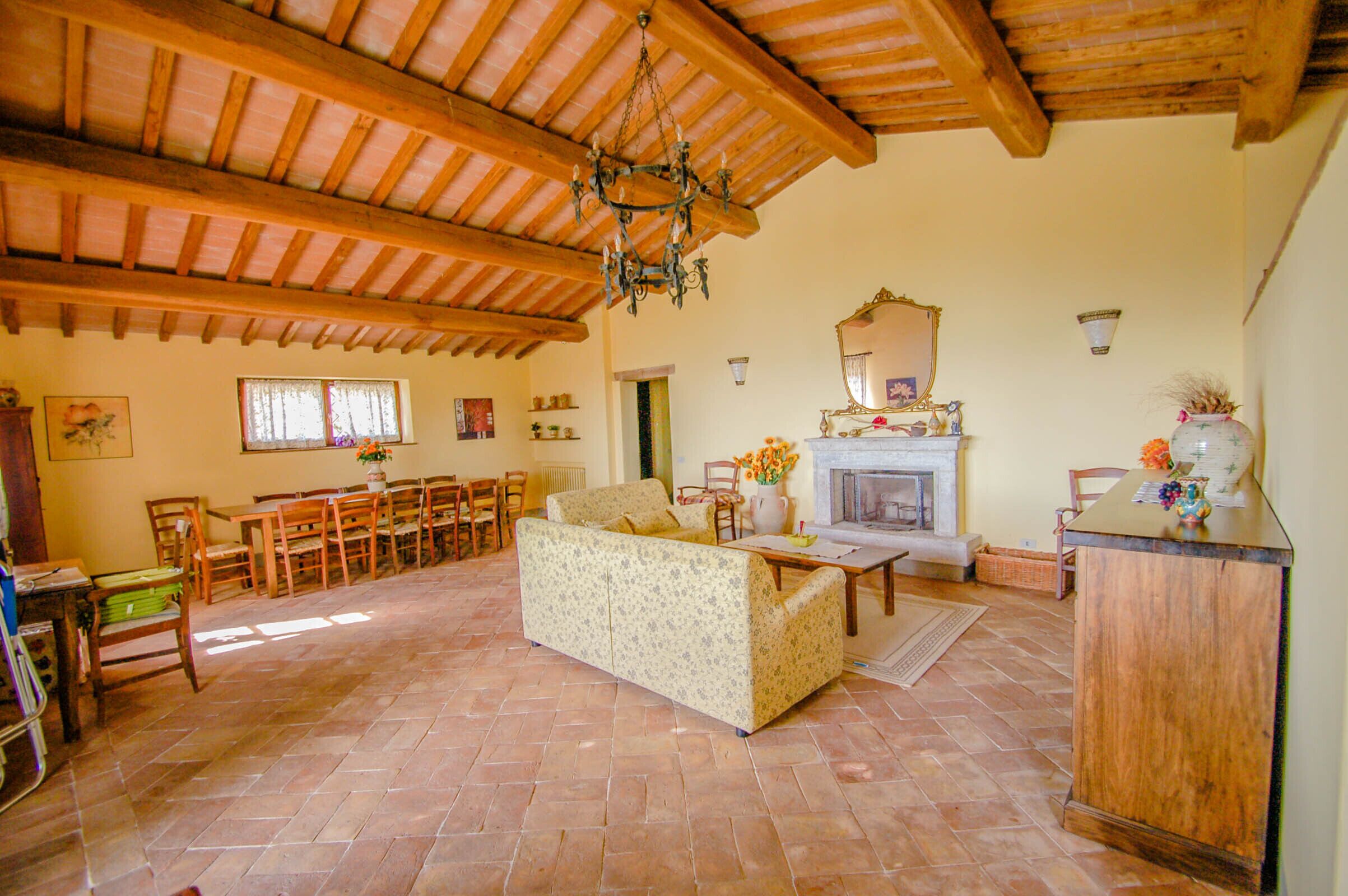 A spacious living room with a high wooden ceiling, a fireplace, a sofa, and a dining area with chairs and a table.