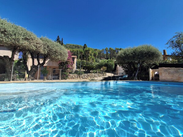 A clear blue swimming pool surrounded by trees and a stone wall.