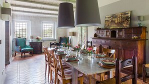 Une salle à manger avec une table en bois dressée pour six personnes, entourée de chaises. Deux grands luminaires sont suspendus au-dessus de la table.
