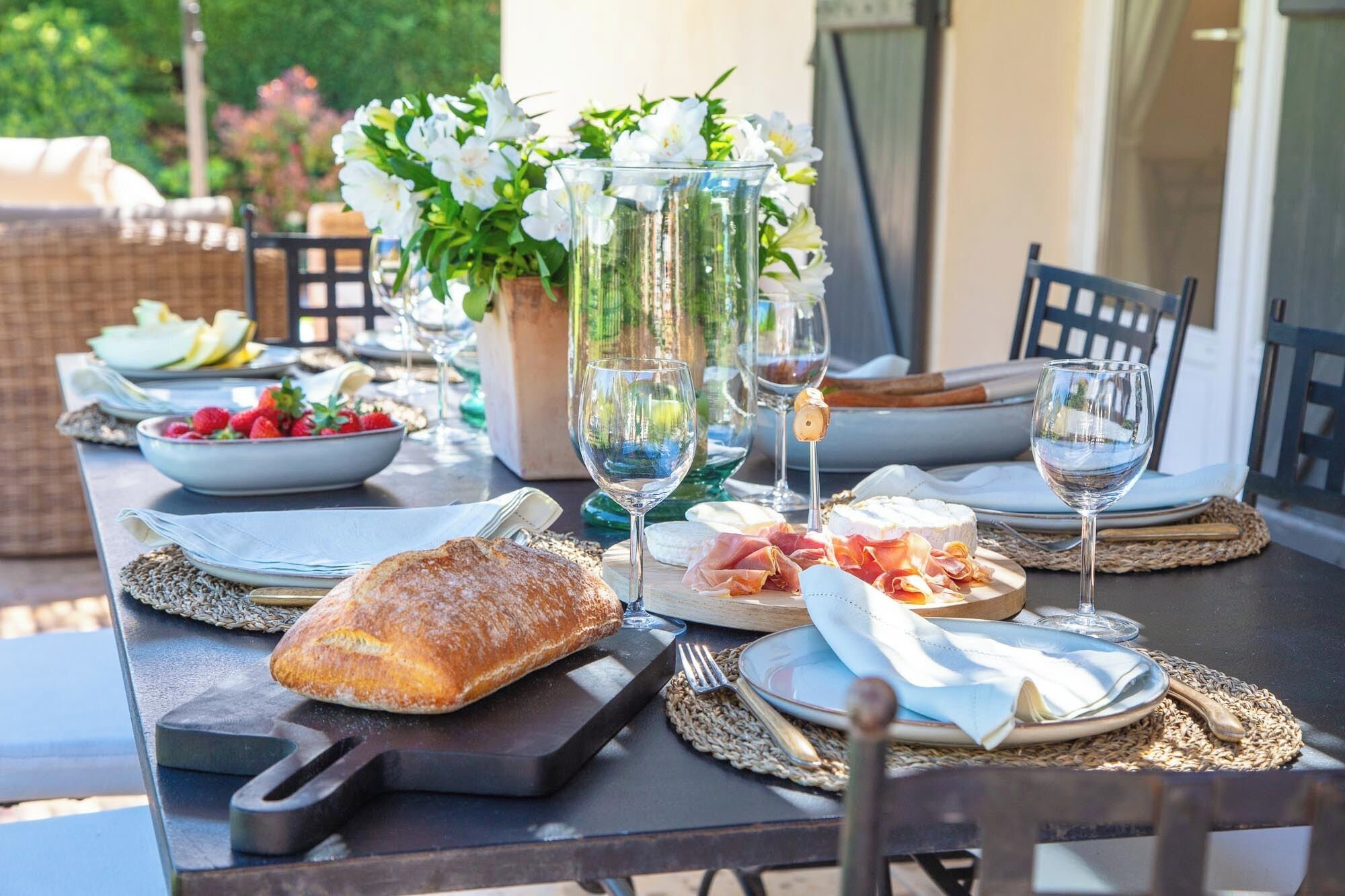 A table set for a meal with plates, glasses, a loaf of bread, and a bowl of fruit.