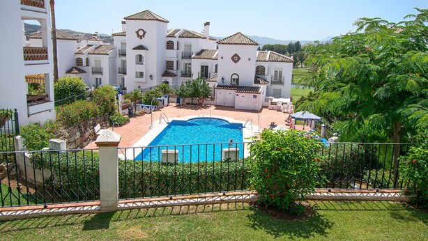 A large white building with a swimming pool, surrounded by greenery and a fenced area. - Stunning Penthouse on Mijas golf course with spectacular mountain views (Malaga)