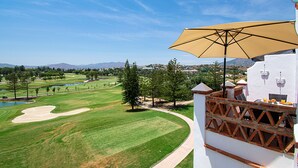 A golf course with a white building featuring a large umbrella and a view of the surrounding landscape. - Stunning Penthouse on Mijas golf course with spectacular mountain views (Malaga)