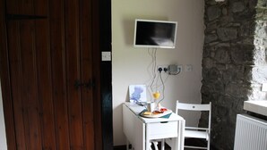 A small room with a stone wall, a white table with breakfast items, a white chair, and a mounted TV. - The Wee Hoose: Probably Scotland's Smallest Holiday Home  (Callander)