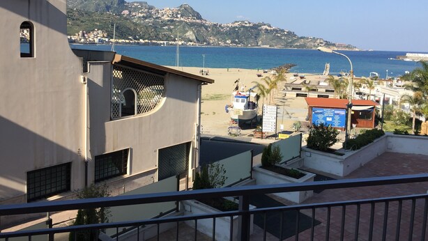 A coastal view with a building in the foreground, a beach, and a mountainous backdrop. - Panoramic studio next to the beach (Giardini Naxos)