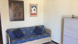 A room with a sofa, a cabinet, and two framed artworks on the wall. - Panoramic studio next to the beach (Giardini Naxos)