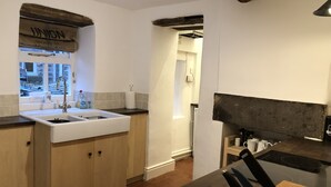 Une cuisine avec un évier blanc, des placards en bois, une fenêtre donnant sur un beau paysage et un plan de travail sur lequel se trouve une bouilloire.
