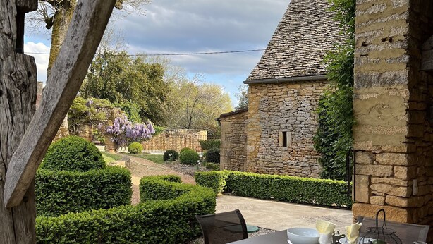 Un espace extérieur aménagé pour les repas, avec des murs en pierre et une vue sur un jardin.