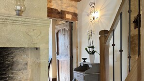 Un intérieur rustique avec une cheminée en pierre, un escalier en bois et un mur décoratif agrémenté d’un luminaire.
