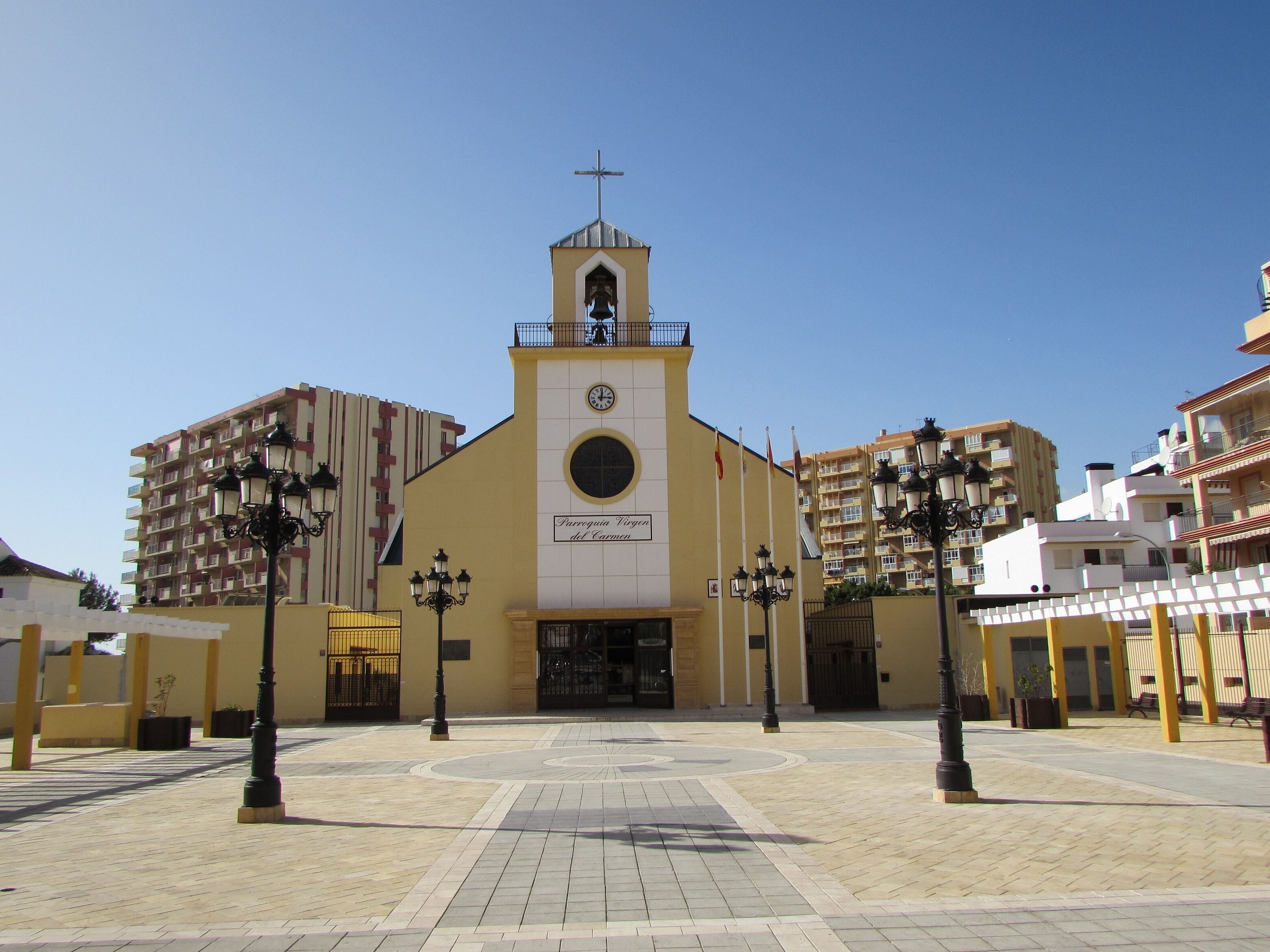 Una iglesia con un campanario, rodeada por una plaza empedrada con faroles.