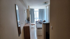 A hallway leading to a living area with a sofa, a coffee table, and a TV. There is a wooden desk with drawers and a mirror on the left. - Studio Apartment, Sleeps 2. Centrally located & close to all amenities. (Benalmádena)