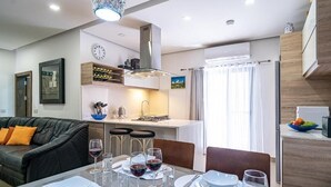 A modern living room with a dining area, a sofa, a coffee table, and a kitchen in the background. -  Apartment with balcony and sea views, fully A/c (Marsalforn)