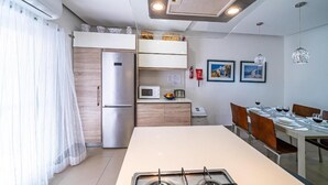 A compact kitchen with a refrigerator, microwave, and gas stove. There is a dining area with a table and chairs. -  Apartment with balcony and sea views, fully A/c (Marsalforn)